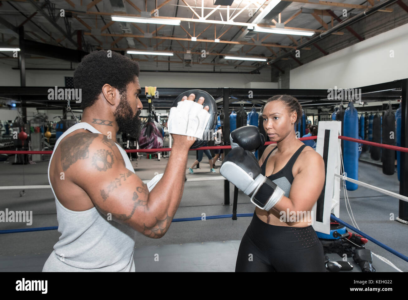 Femme noire qui fait un sparring avec un entraîneur dans un ring de boxe Banque D'Images