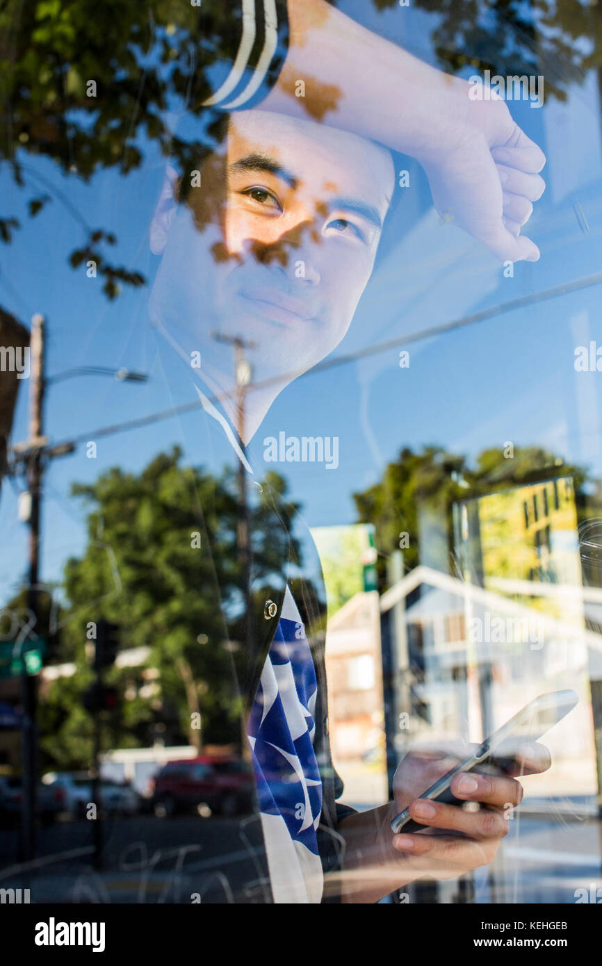 Homme chinois souriant, pendu sur la fenêtre tenant le téléphone portable Banque D'Images