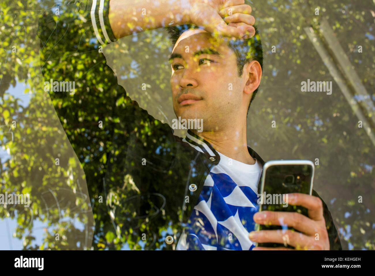 Un sérieux Chinois qui se penche sur la fenêtre tenant un téléphone portable Banque D'Images