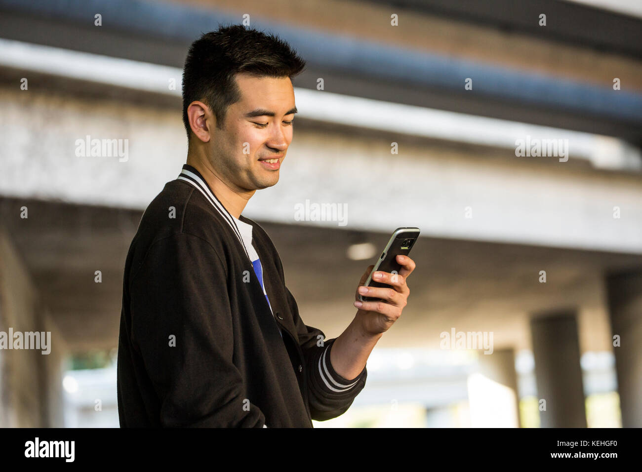 Homme chinois souriant envoyant un SMS sur un téléphone portable Banque D'Images