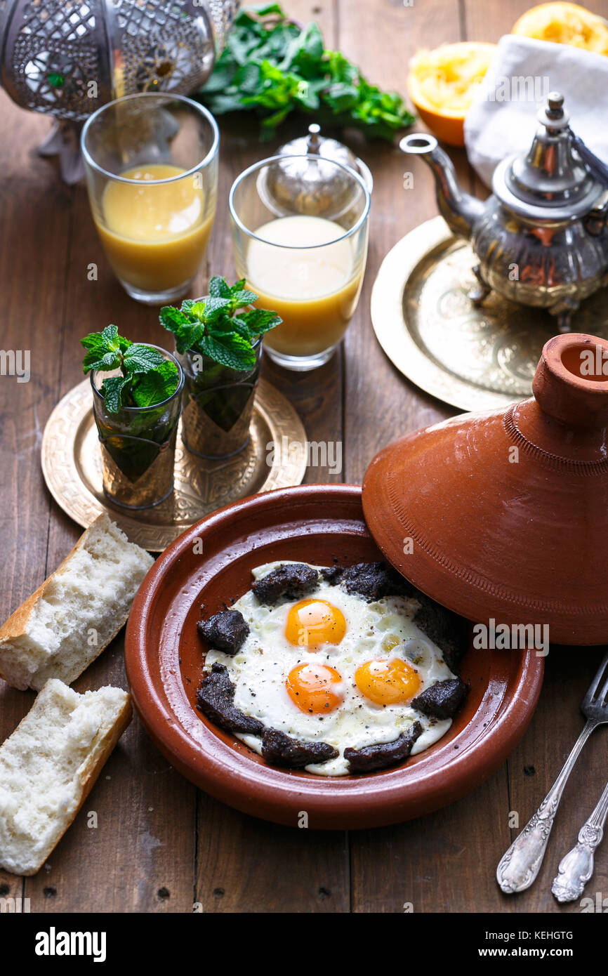 Sunnyside œufs cuits dans un plat à tajine boeuf, petit-déjeuner marocain avec du jus de fruit et thé à la menthe. Banque D'Images