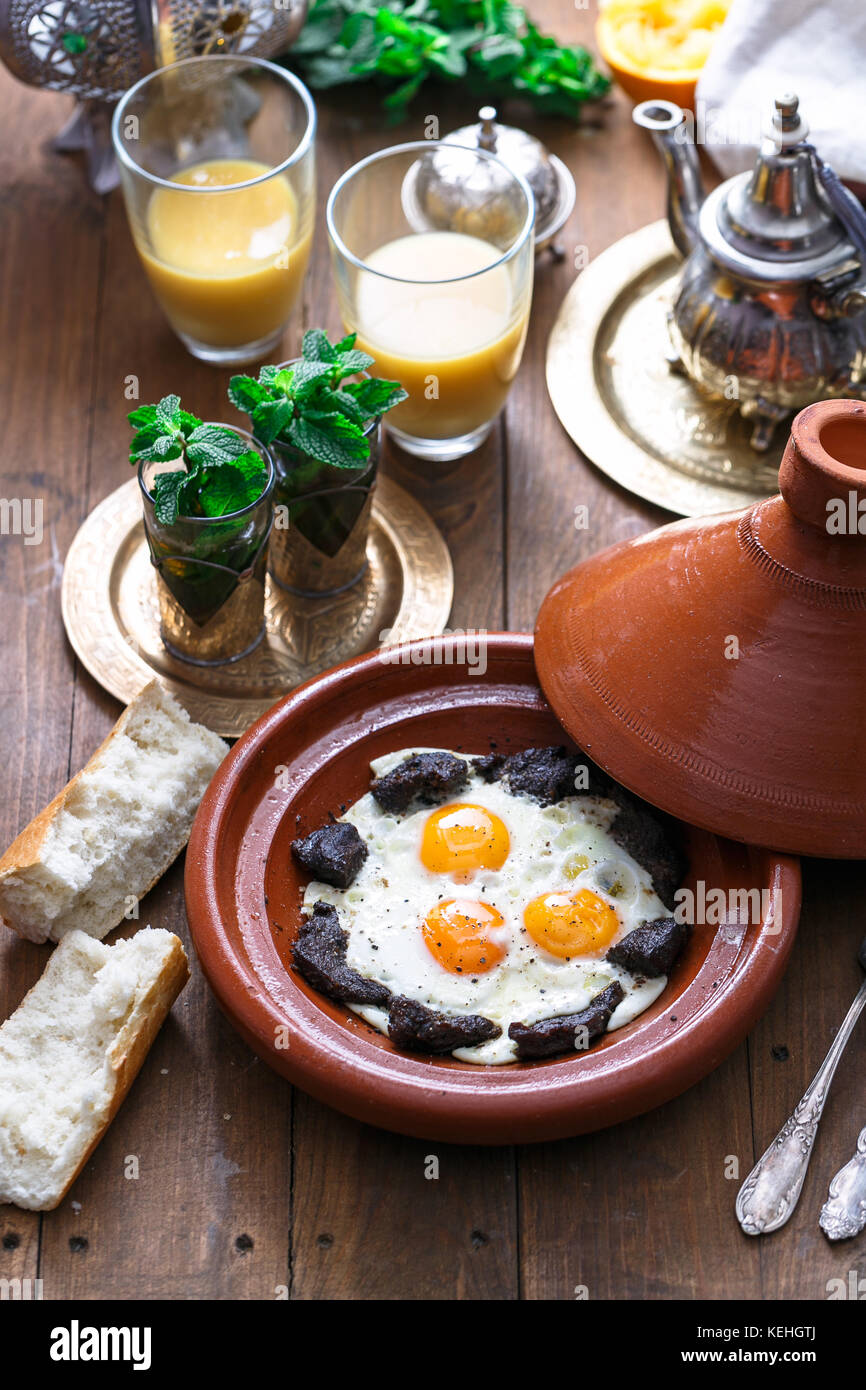 Sunnyside œufs cuits dans un plat à tajine boeuf, petit-déjeuner marocain avec du jus de fruit et thé à la menthe. Banque D'Images