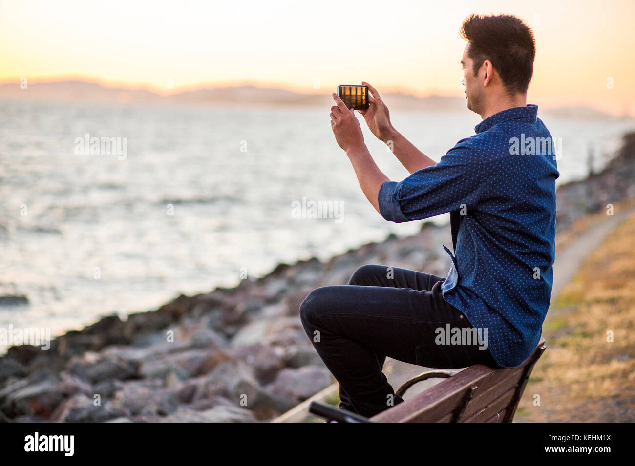 Homme chinois assis sur un banc pour photographier l'océan avec un téléphone portable Banque D'Images