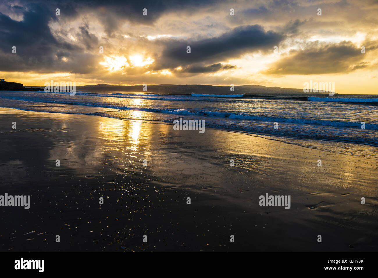 Gwithian Beach, St Ives, Cornouailles. Une soirée orageuse avec une lumière puissante du soleil couchant. La pluie et la marée ont trempé le sable de la plage pour en faire un miroir. Banque D'Images