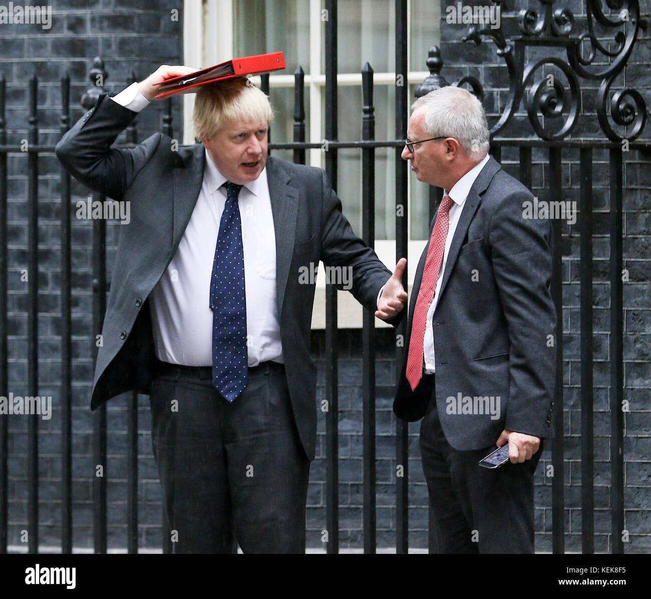 Boris Johnson à Downing Street sort sous la pluie à l'aide de son dossier pour le protéger de la météo Banque D'Images