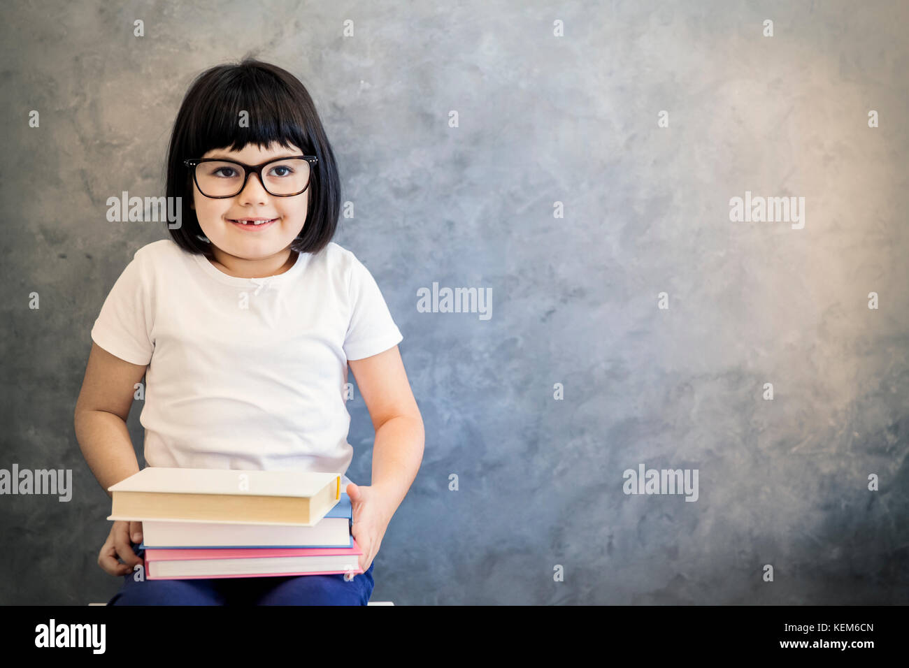 Portrait of cute little girl cheveux noirs avec des lunettes holding books par le mur Banque D'Images