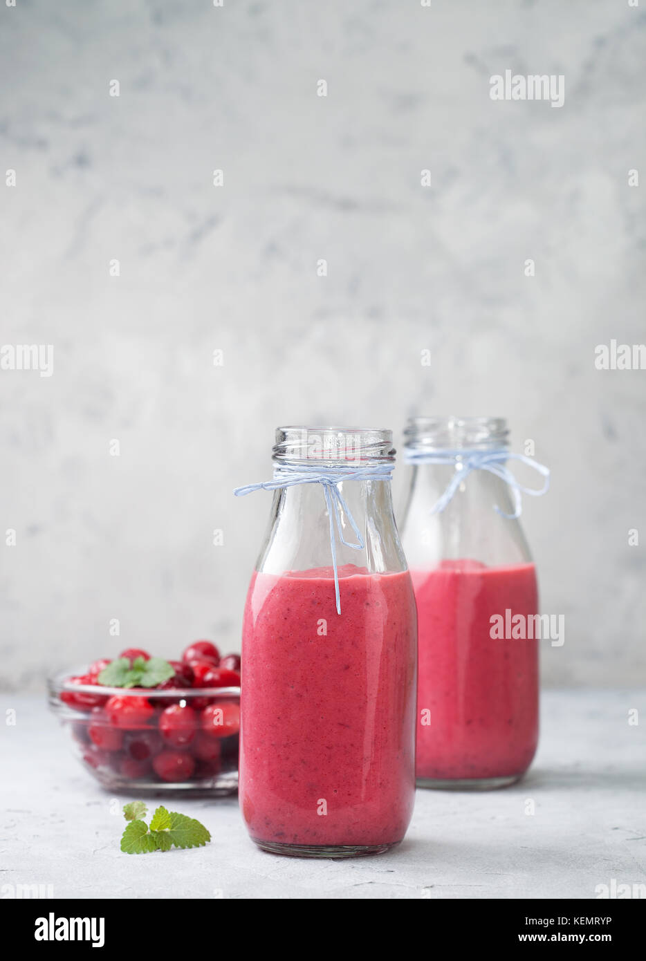 Les smoothies cranberries en bouteilles de verre, les canneberges fraîches dans un bol sur un fond de béton gris Banque D'Images