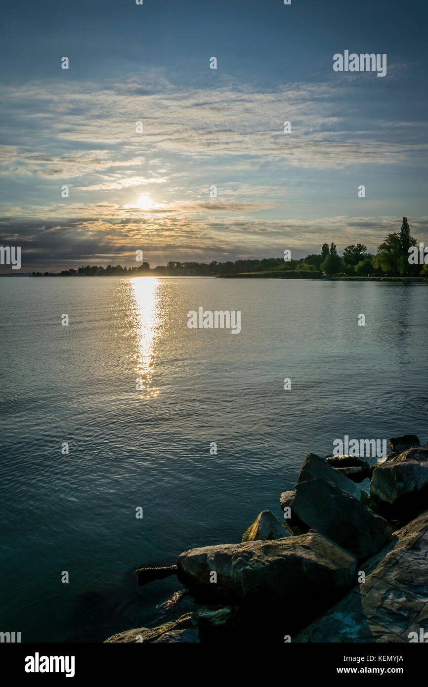 Golden sunrise over lac tranquille, dramatique nuages et ciel. Le soleil levant d'or de lumière venant de derrière les nuages à l'horizon de calme du lac Balaton. Banque D'Images