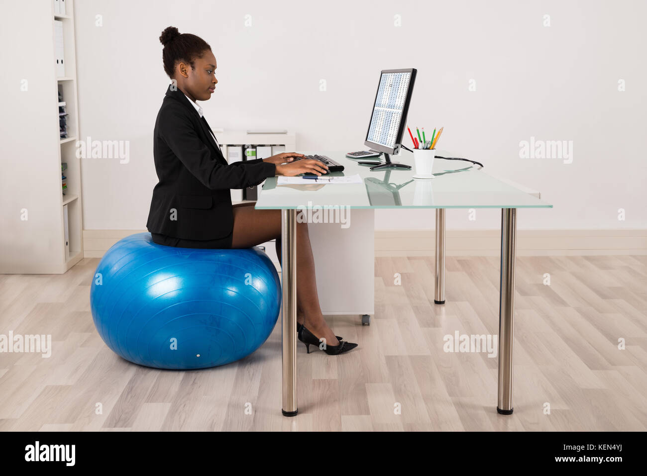 Les jeunes african businesswoman using computer while sitting on fitness ball in office Banque D'Images