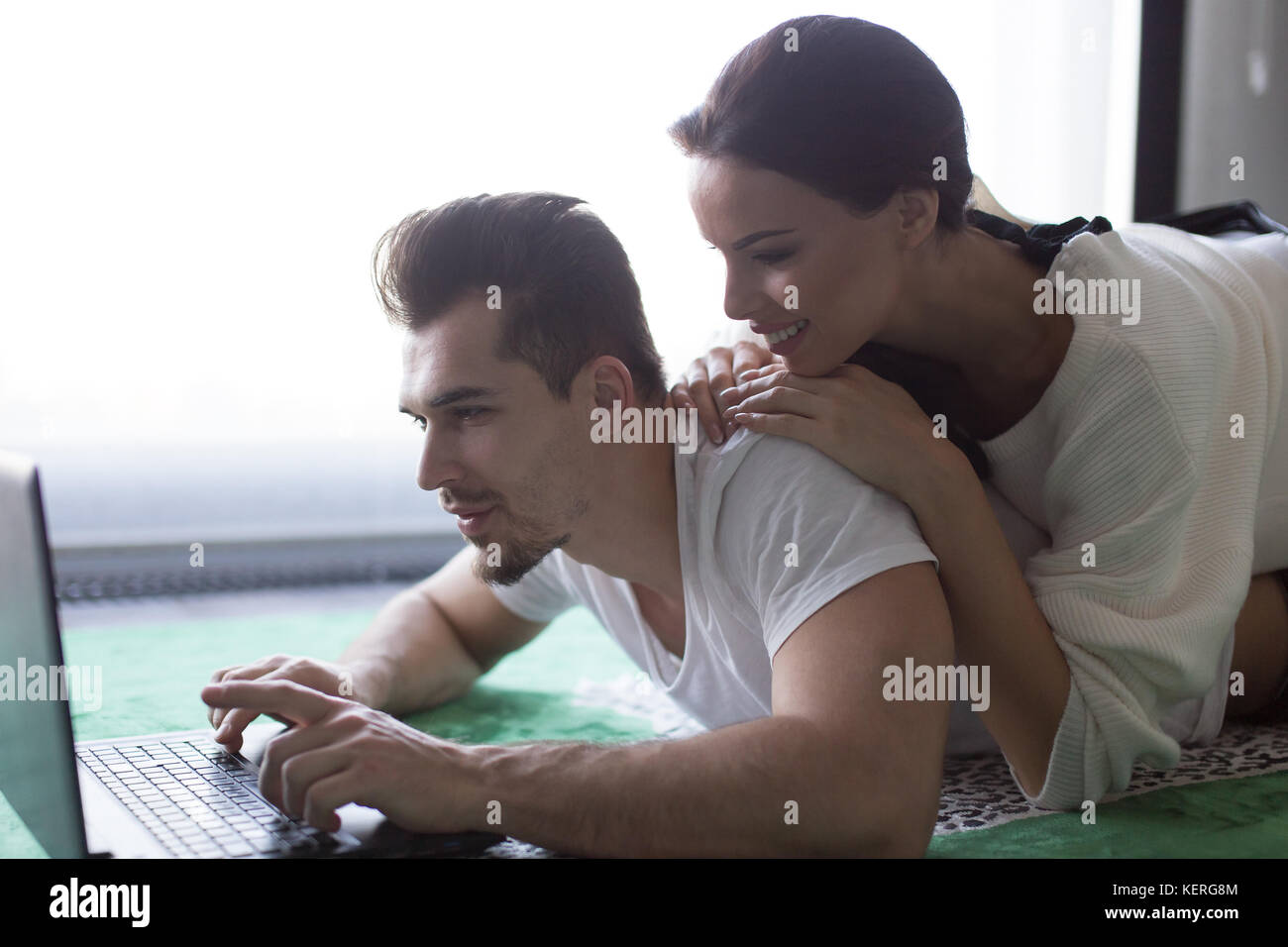 Jeune couple shopping online par ordinateur portable, couché sur un tapis à la maison Banque D'Images