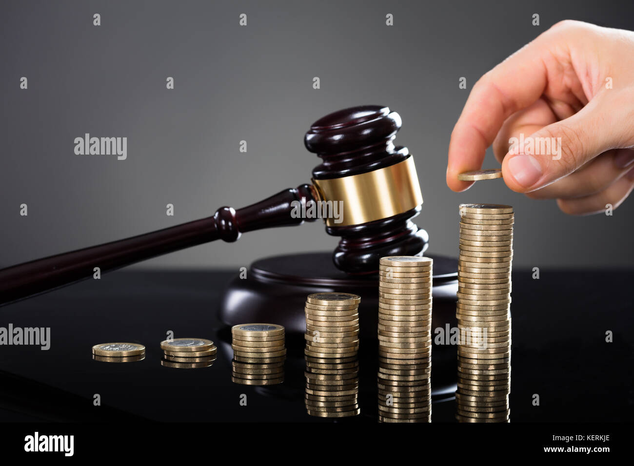 Close-up of a hand stacking coins en face de mallet sur fond gris Banque D'Images