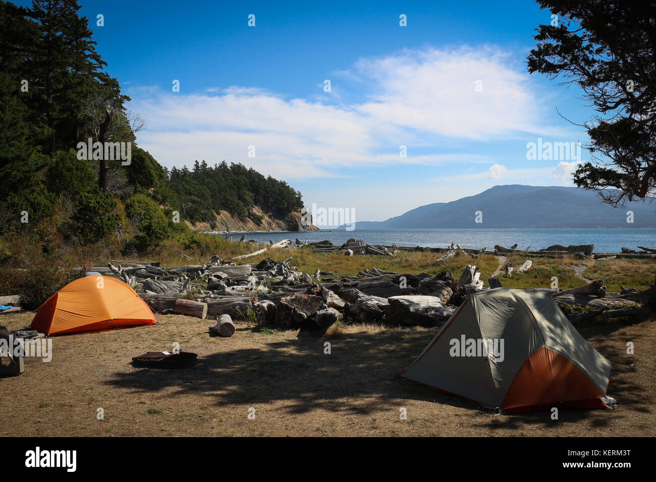 Deux tentes, une orange, l'un gris, sur un terrain de camping sur l'île sucia, état de Washington, avec vue sur le Puget Sound, Orcas Island, les pins sur les falaises ciel bleu, nuage Banque D'Images