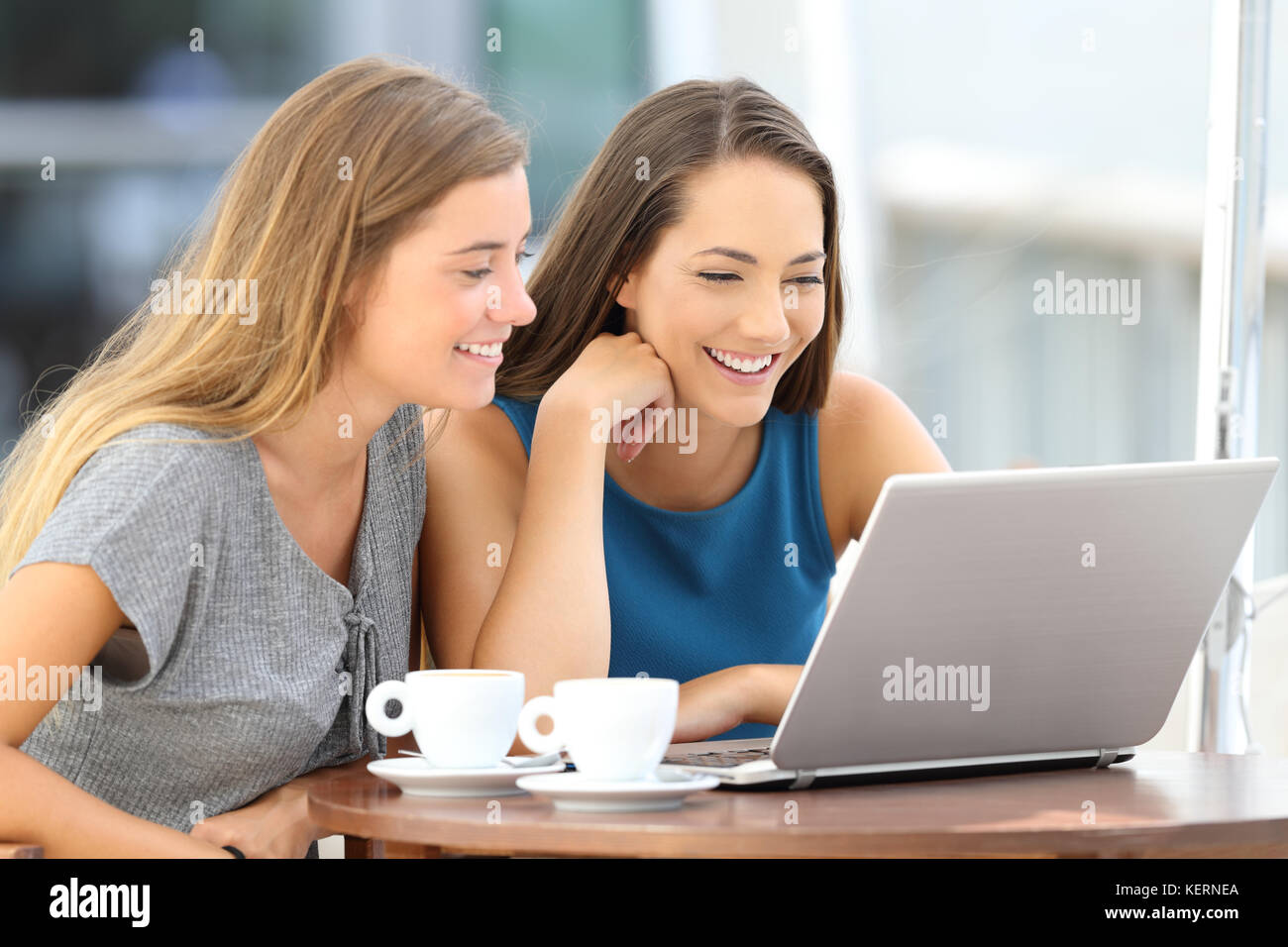 Deux amis heureux regardant le contenu diffusé en ligne dans un ordinateur portable assis dans un bar terrasse Banque D'Images