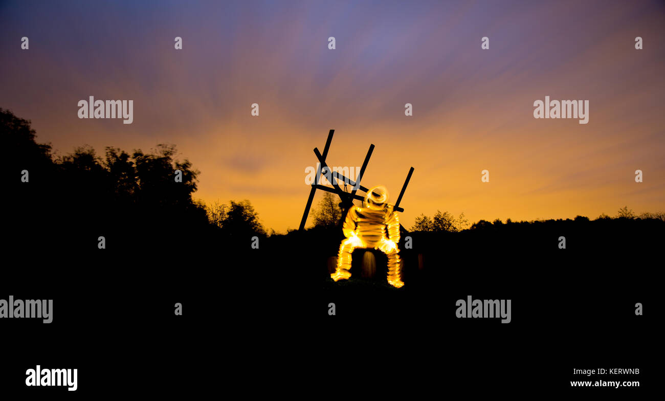 Étrangement, une étrange figure rayonnante assise seule dans le noir avec un ciel atmosphérique au-dessus de lui. Banque D'Images