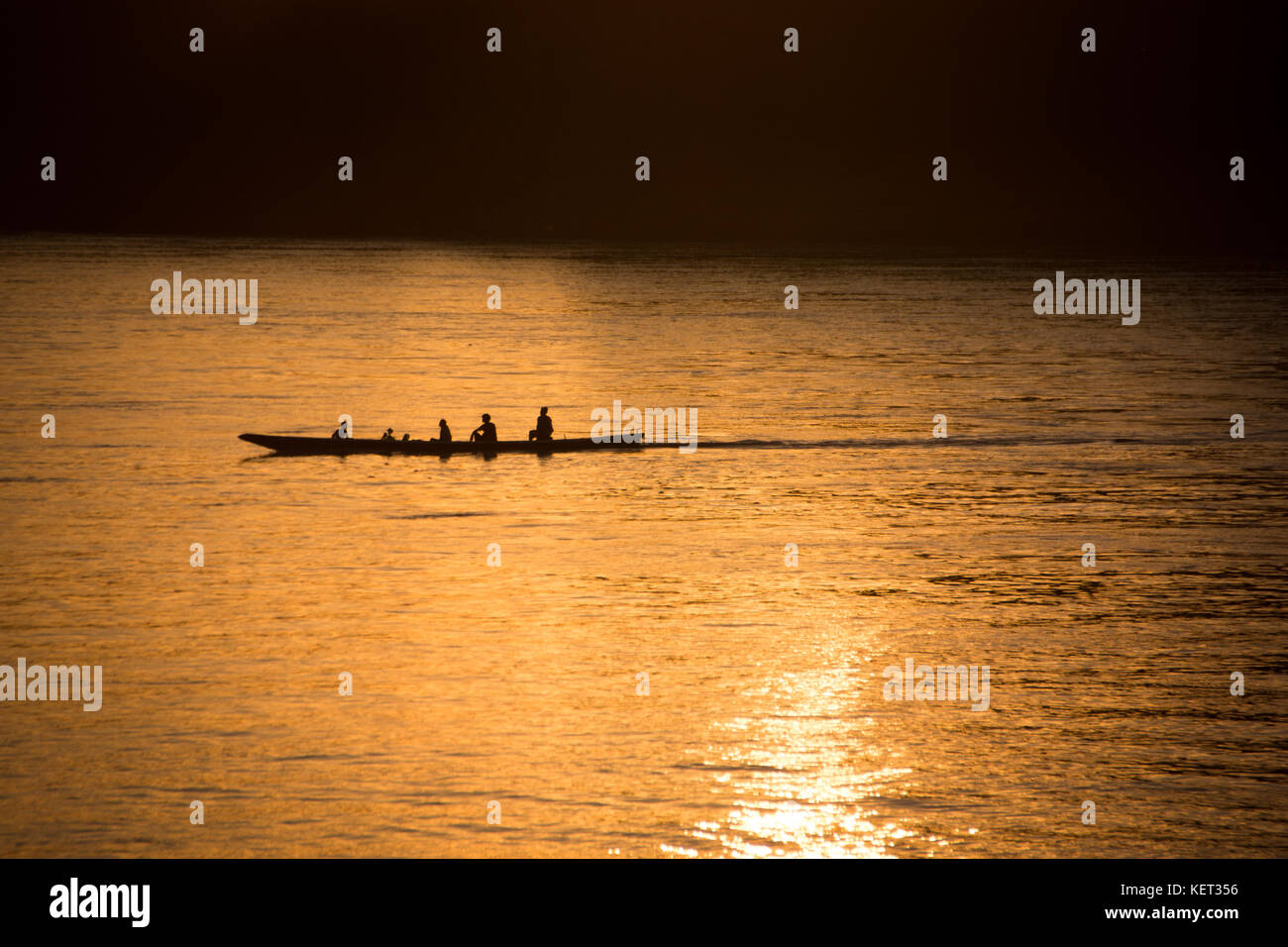 Silhouette d'un bateau flottant de la famille dans le coucher du soleil sur le fleuve du Mékong, au Laos Banque D'Images