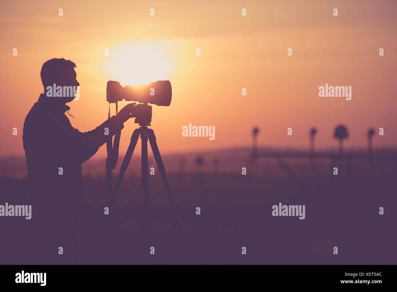 Les hommes prenant les photos à l'extérieur pendant le coucher du soleil. pittoresque silhouette photographe. téléobjectif et moderne de l'appareil sur un pied. Banque D'Images