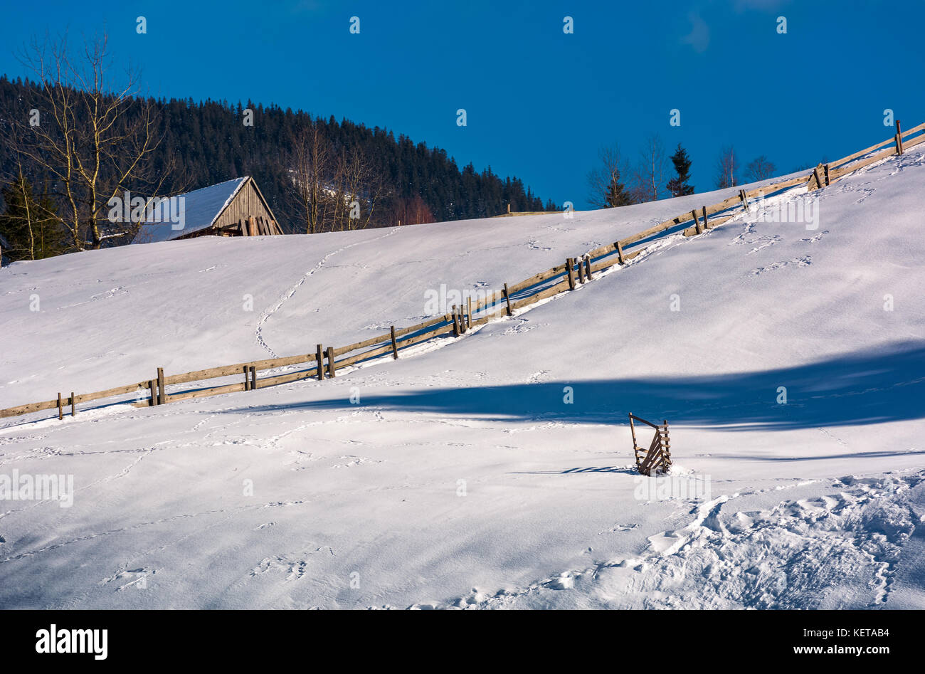 Bûcher au-dessus de la colline de neige avec clôture en bois. jolie paysage rural montagneux Banque D'Images