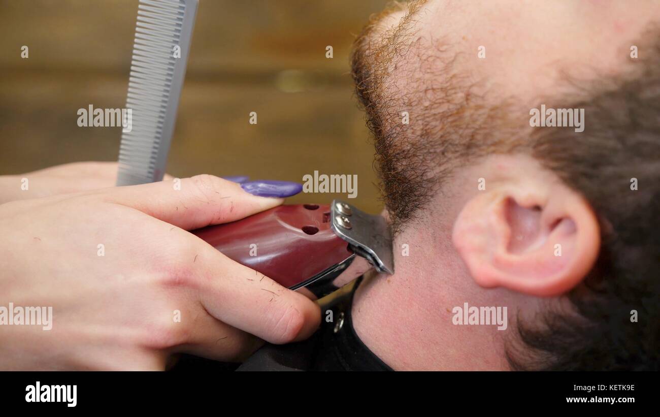 Coiffeur professionnel avec barbe rasage rasoir machine. Vue de côté  portrait de beau jeune homme barbu se coupe de la mode moderne dans un  salon de barbier salon de coiffure attrayante. travail