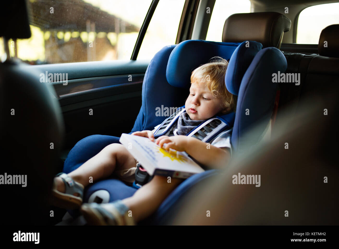 Petit garçon assis dans le siège auto dans la voiture, tenant un livre. Banque D'Images