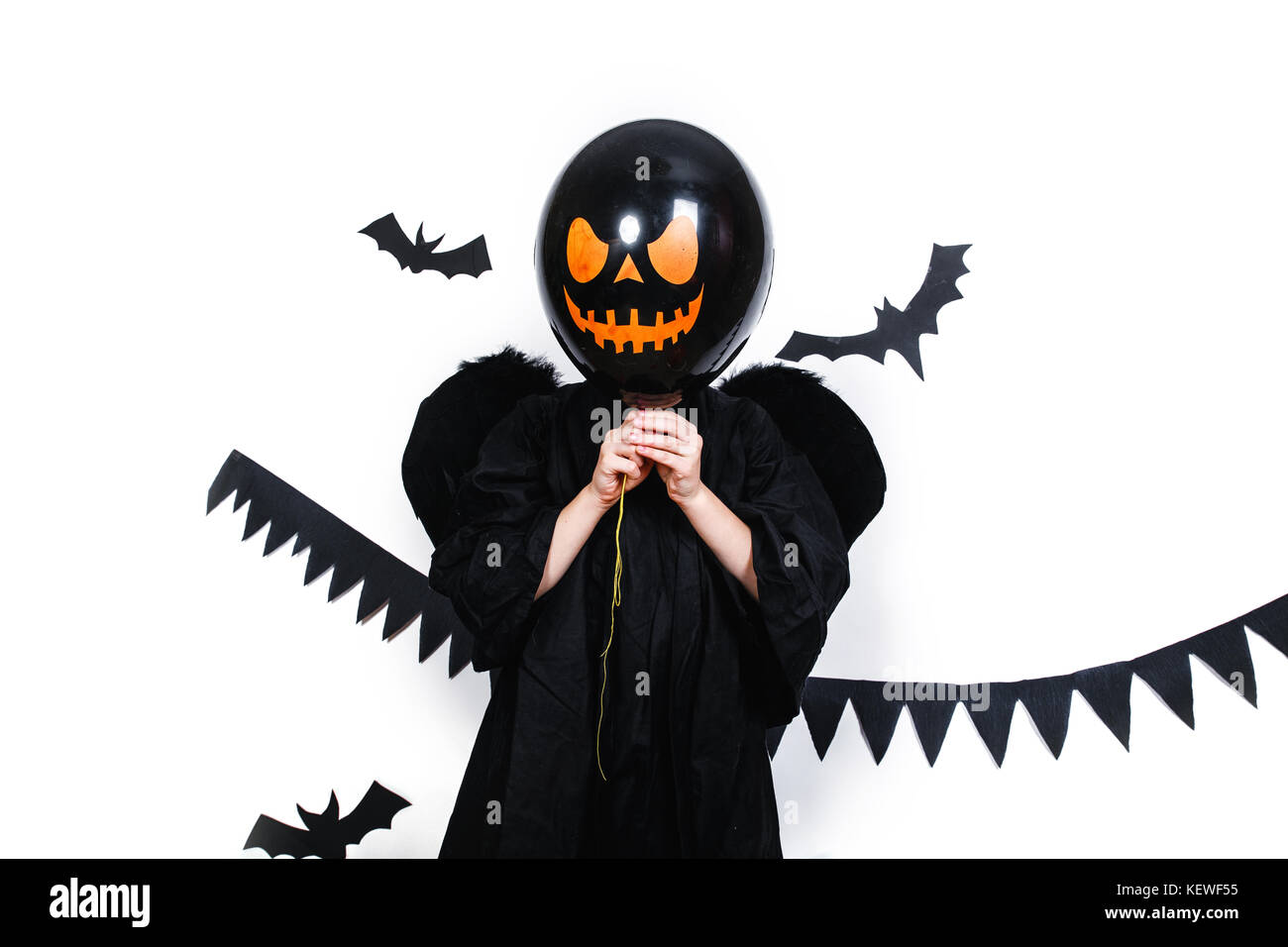 Garçon vêtu comme un ange tenant un ballon noir en face de son visage. Banque D'Images