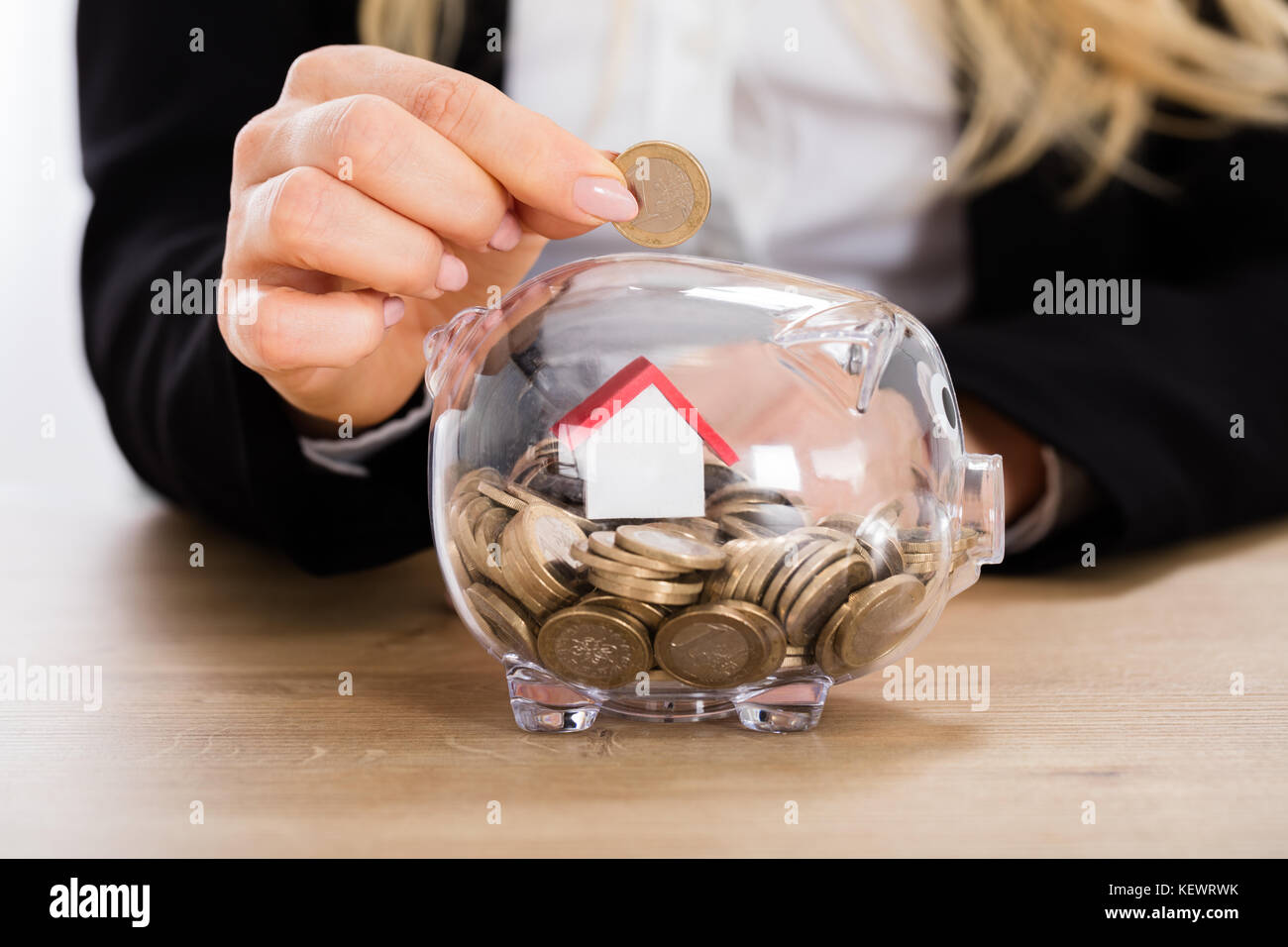 L'insertion d'une pièce de monnaie pour femme tirelire transparente remplie de pièces de monnaie et la maison modèle. Concept d'investissement immobilier Banque D'Images