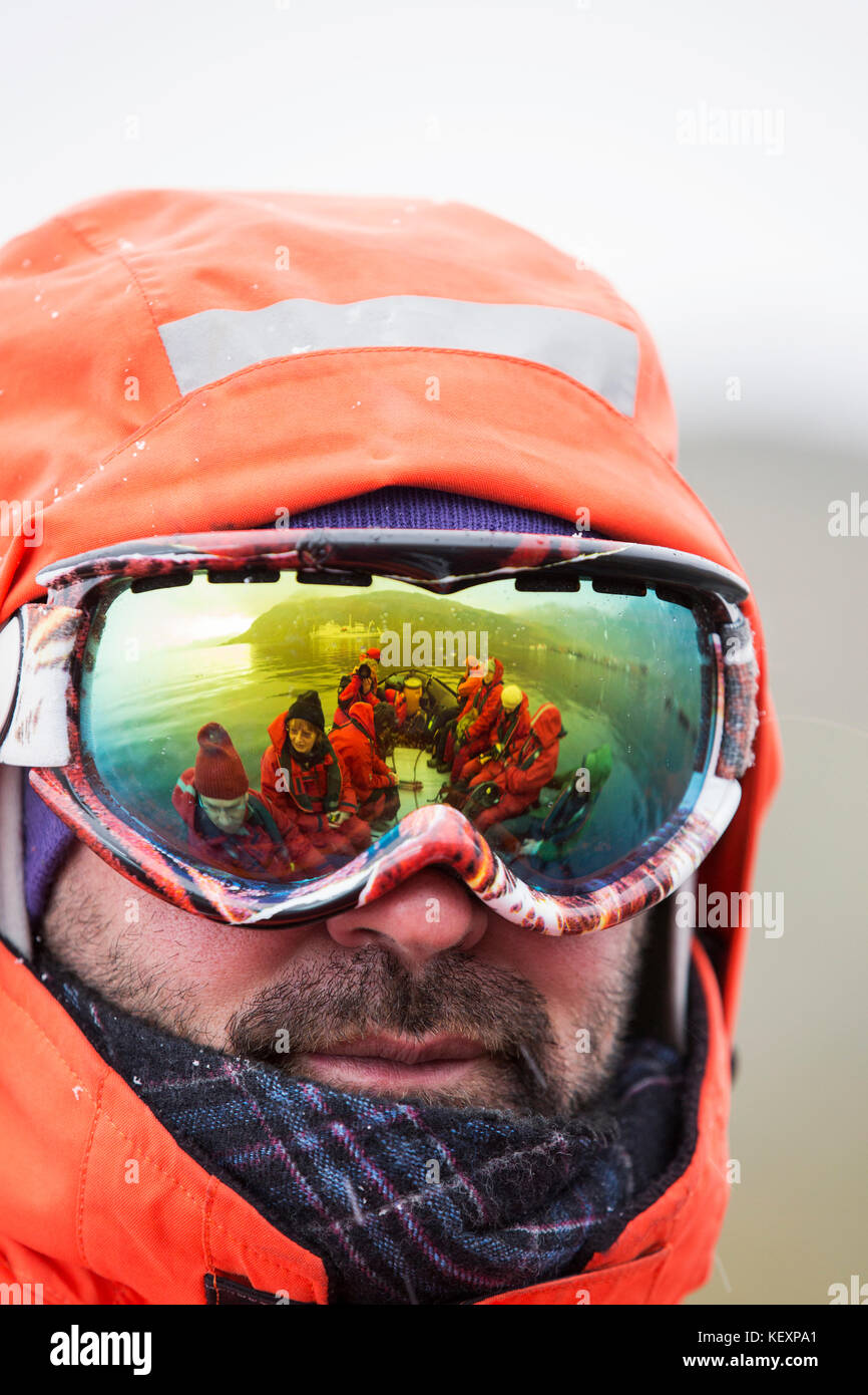 Membres d'une expédition en Antarctique croisière s'élancer depuis la plaine de Salisbury en Géorgie du Sud dans un Zodiak de retourner à l'expedition cruise ship, reflétée dans les lunettes d'un instructeur. Banque D'Images