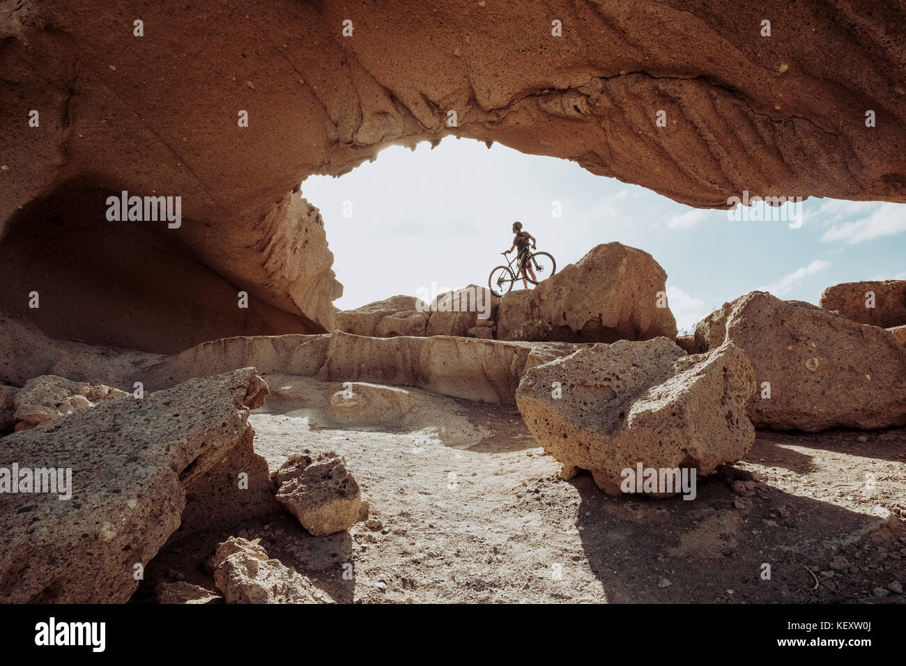 Homme debout avec son vélo de montagne sous une grande arche de roche, Ténérife, îles Canaries, Espagne Banque D'Images