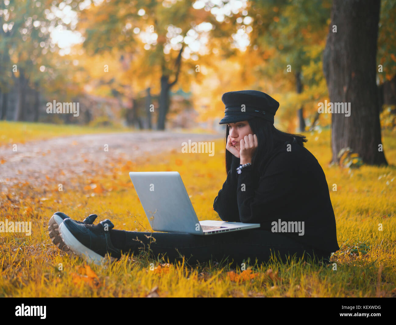 Young woman using laptop piscine assis sur l'herbe jaune et souriant. girl using digital tablet pc dans le parc. student après l'école. Banque D'Images