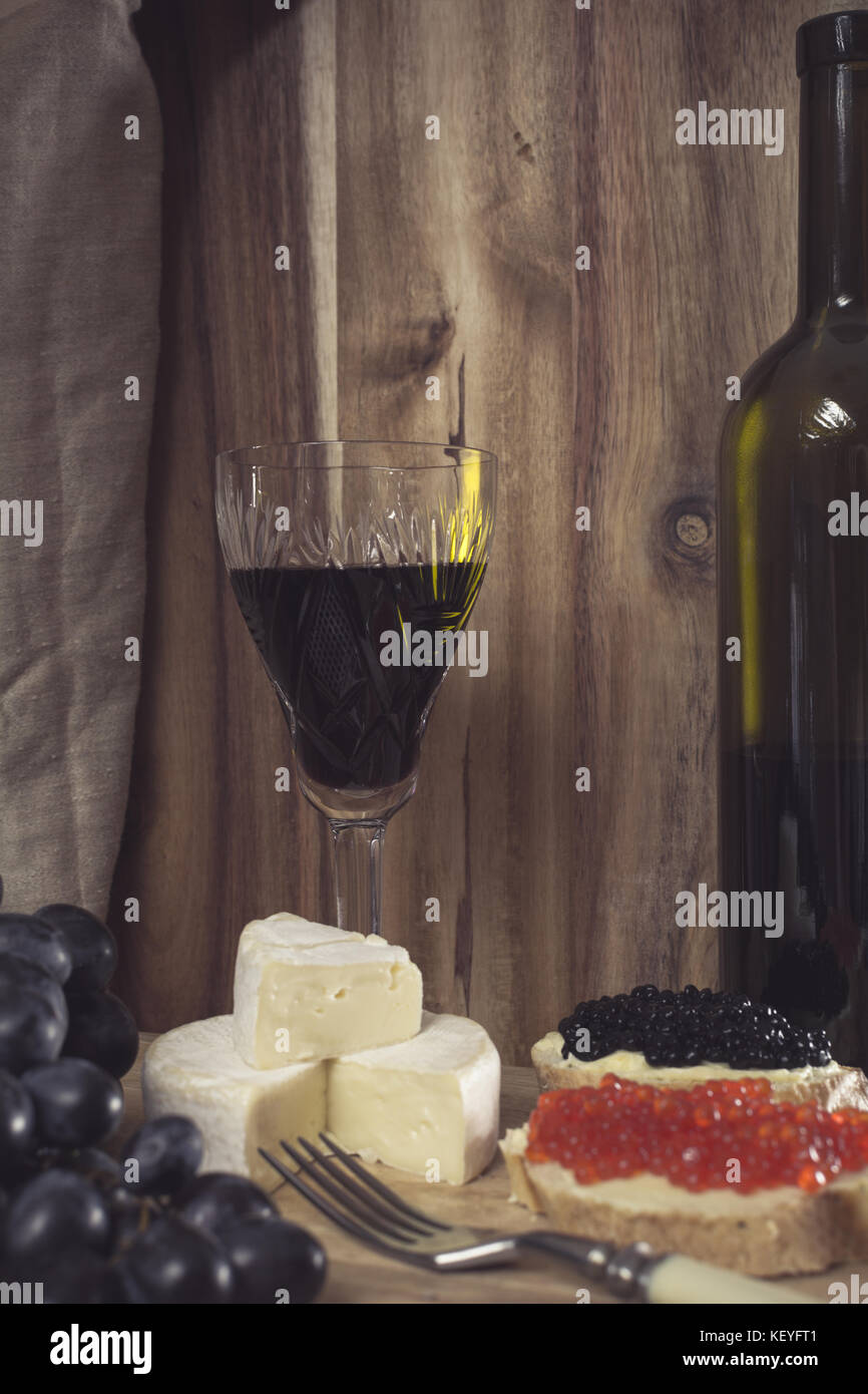 Un verre de vin rouge, fromage brie, raisins et du caviar Banque D'Images