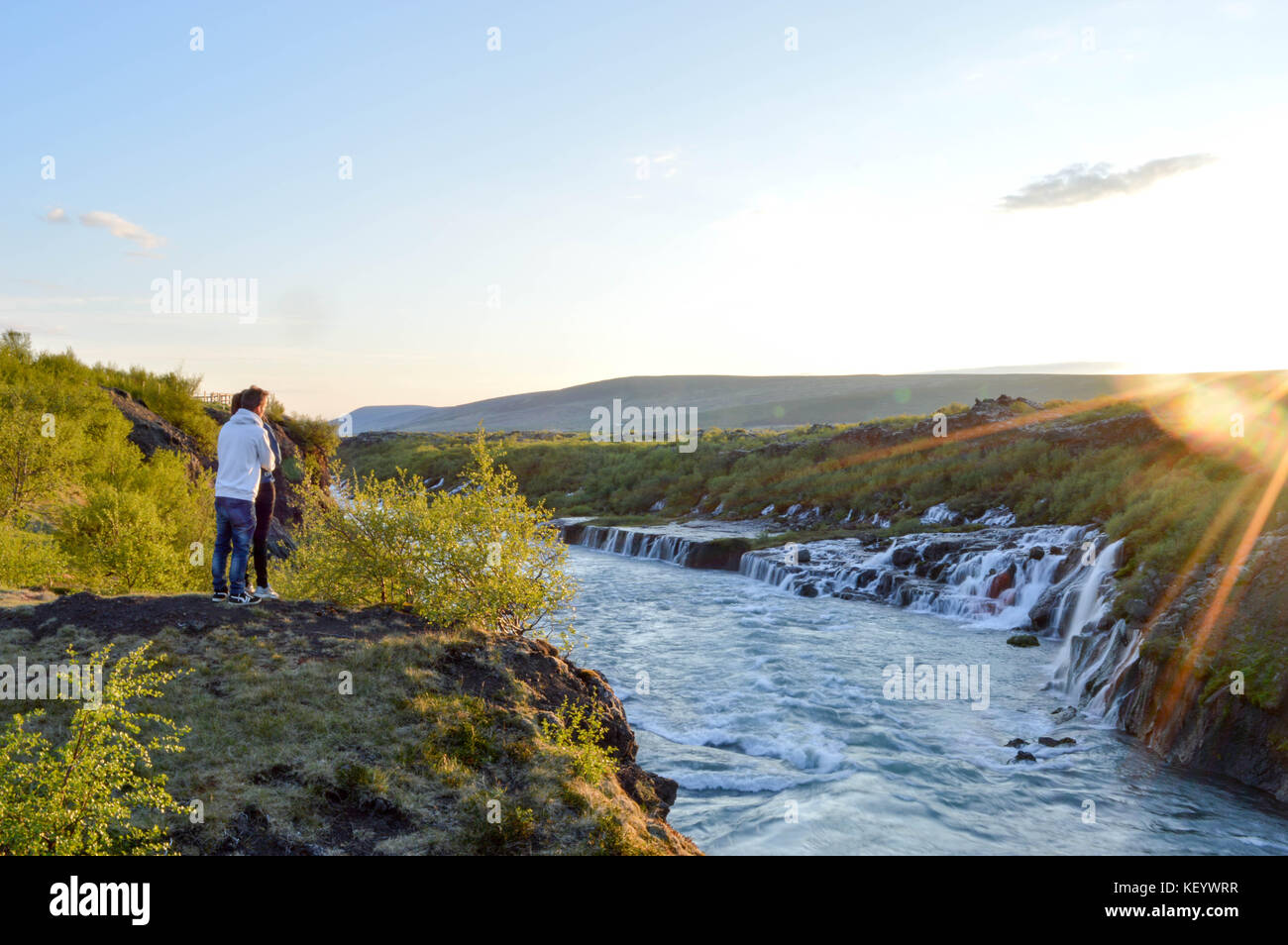 Couple amoureux appréciant le coucher du soleil dans l'ouest de l'Islande par la chute d'eau de Hraunfossar Banque D'Images