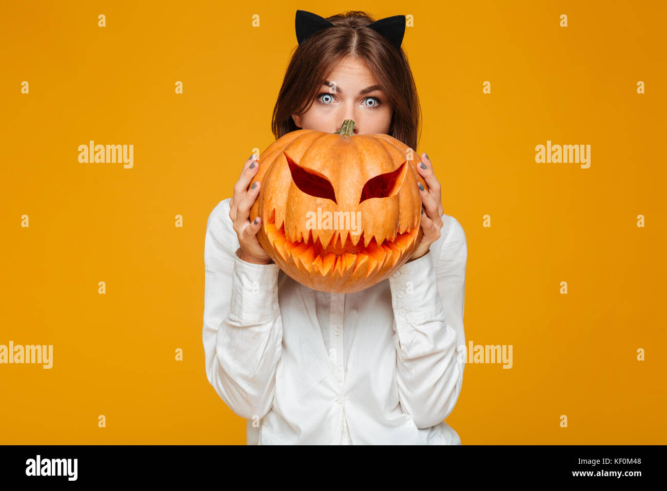 Photo de jeune femme choquée habillés en costume halloween chat fou sur fond jaune avec des citrouilles. Banque D'Images