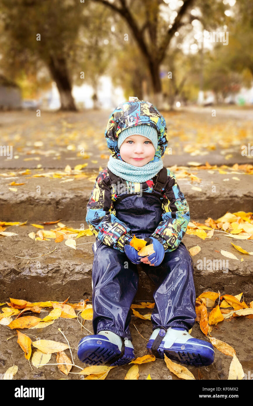 Un enfant, un garçon est assis sur les marches, une promenade dans l'automne sous la pluie Banque D'Images