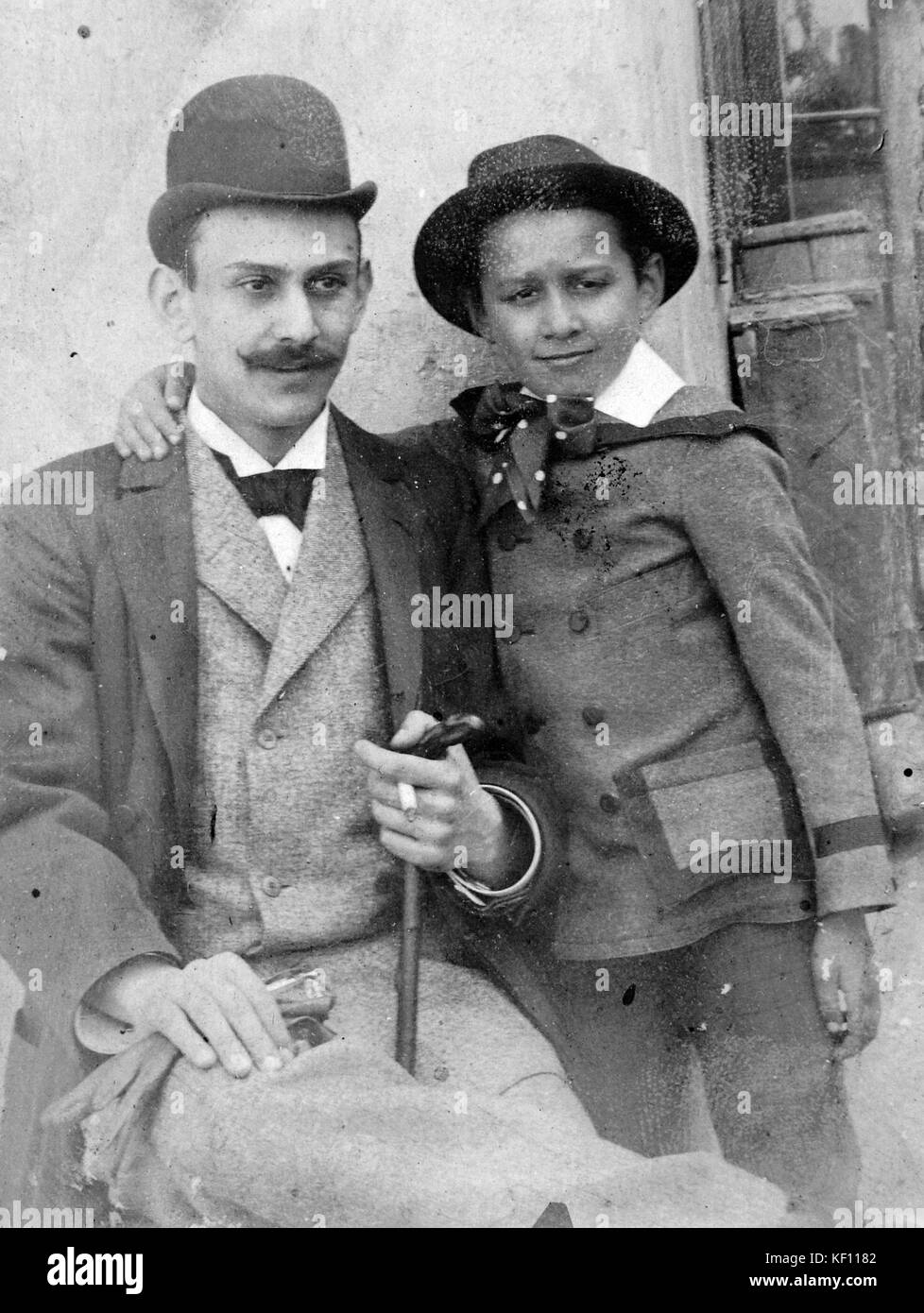 Photographie en noir et blanc représentant un homme et un enfant, montrant leur posture, l'homme portant un chapeau et fumant. Cette image capture la vie quotidienne au début du XXe siècle. Banque D'Images