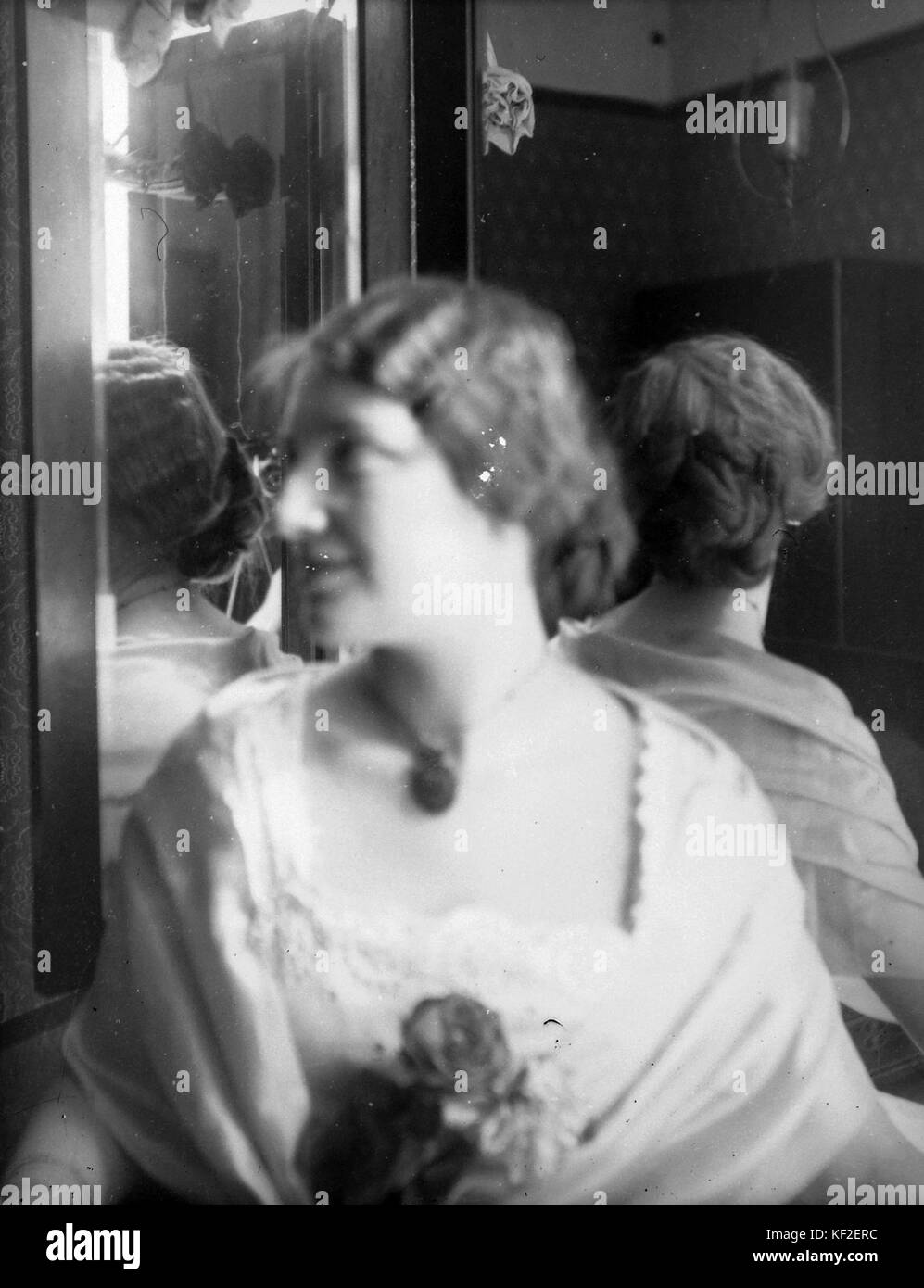 Portrait d’une femme capturée dans un moment de réflexion, regardant dans un miroir avec une fleur à la main, mettant en valeur son image et le reflet d’une manière délicate et artistique. Banque D'Images