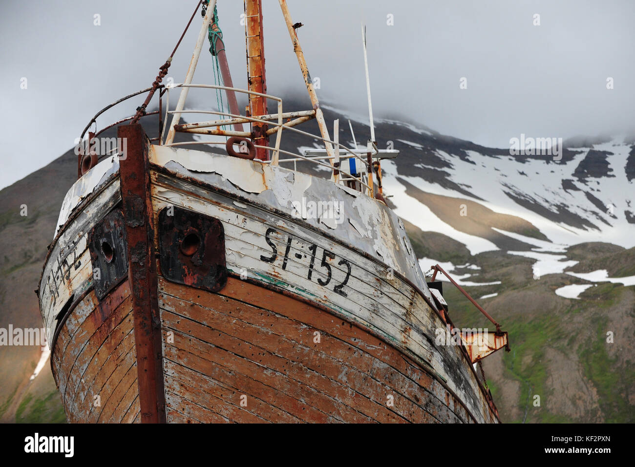 Bateau rouillé abandonné altérées avec l'écaillage de la peinture en ship yard de siglufjordur ville à distance avec des montagnes enneigées en arrière-plan, le nord de l'islande Banque D'Images