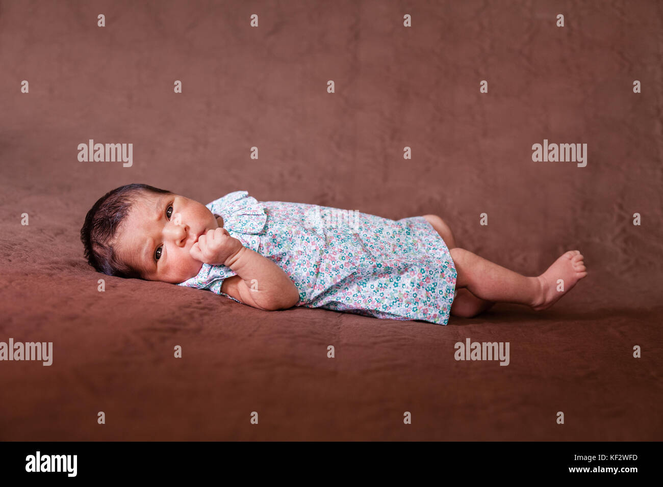 Cute deux semaines Naissance bebe Fille allongée, les yeux ouverts et à la recherche autour de porter une robe florale / Naissance bebe Fille couché lit enfant yeux Banque D'Images
