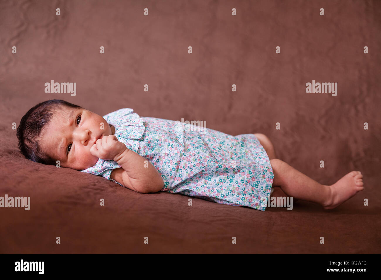 Cute deux semaines Naissance bebe Fille allongée, les yeux ouverts et à la recherche autour de porter une robe florale / Naissance bebe Fille couché lit enfant yeux Banque D'Images
