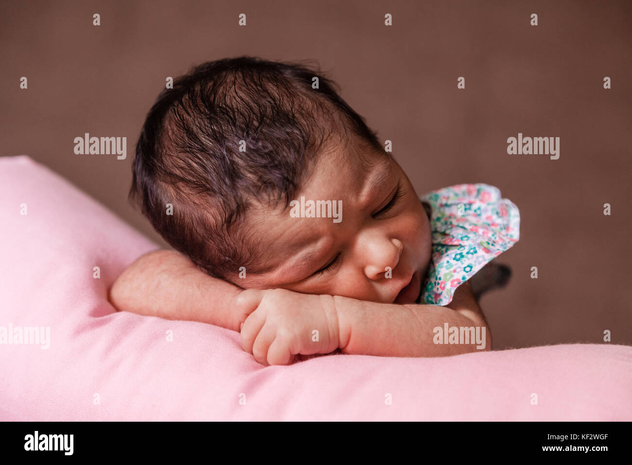 Close up portrait of a cute deux semaines Naissance bebe Fille portant une robe à fleurs, dormir paisiblement sur un oreiller / nouveau-né portrait mignon Banque D'Images