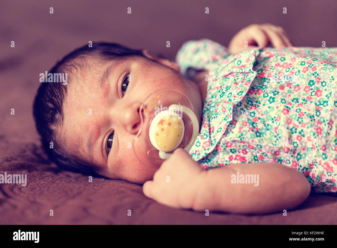 Portrait d'une deux semaines Naissance bebe Fille couchée avec une sucette ou dummy, looking at camera avec une robe à fleurs / sucette nouveau-né dummy Banque D'Images
