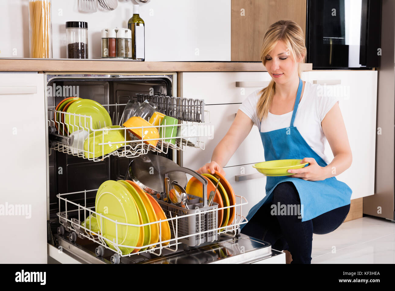 Jeune femme organiser les plaques dans un lave-vaisselle à la maison Banque D'Images