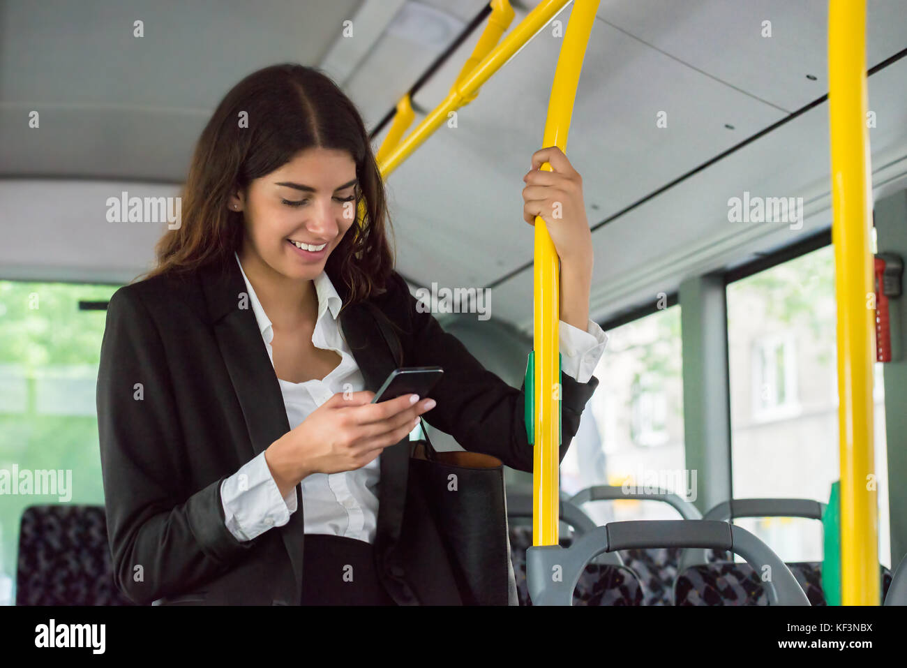 Young smiling businesswoman using smartphone lors de vos déplacements par transports en commun Banque D'Images