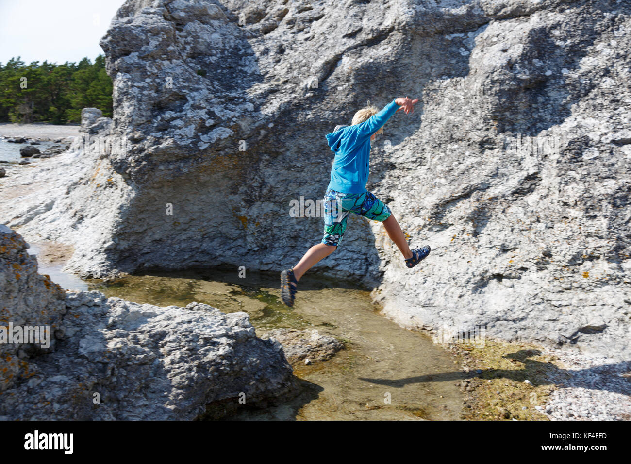 Garçon sautant au-dessus de l'eau entre les rochers à Gotland côte sud est Banque D'Images