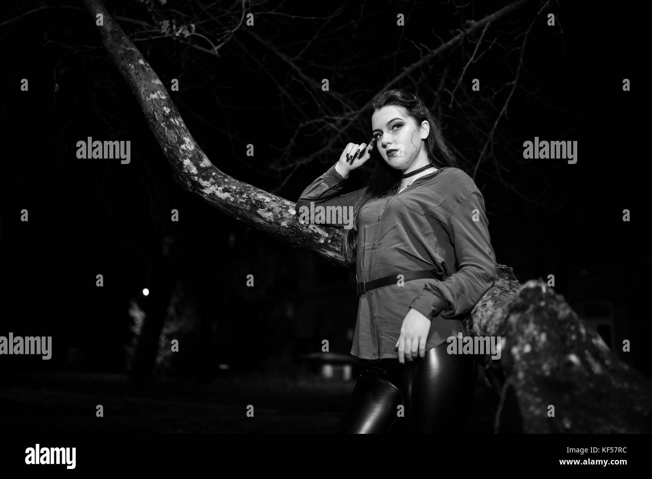 Black Girl in red shirt et lumineuses make-up sur nuit rue assis sur une arbre effrayant. thème de l'halloween. Banque D'Images