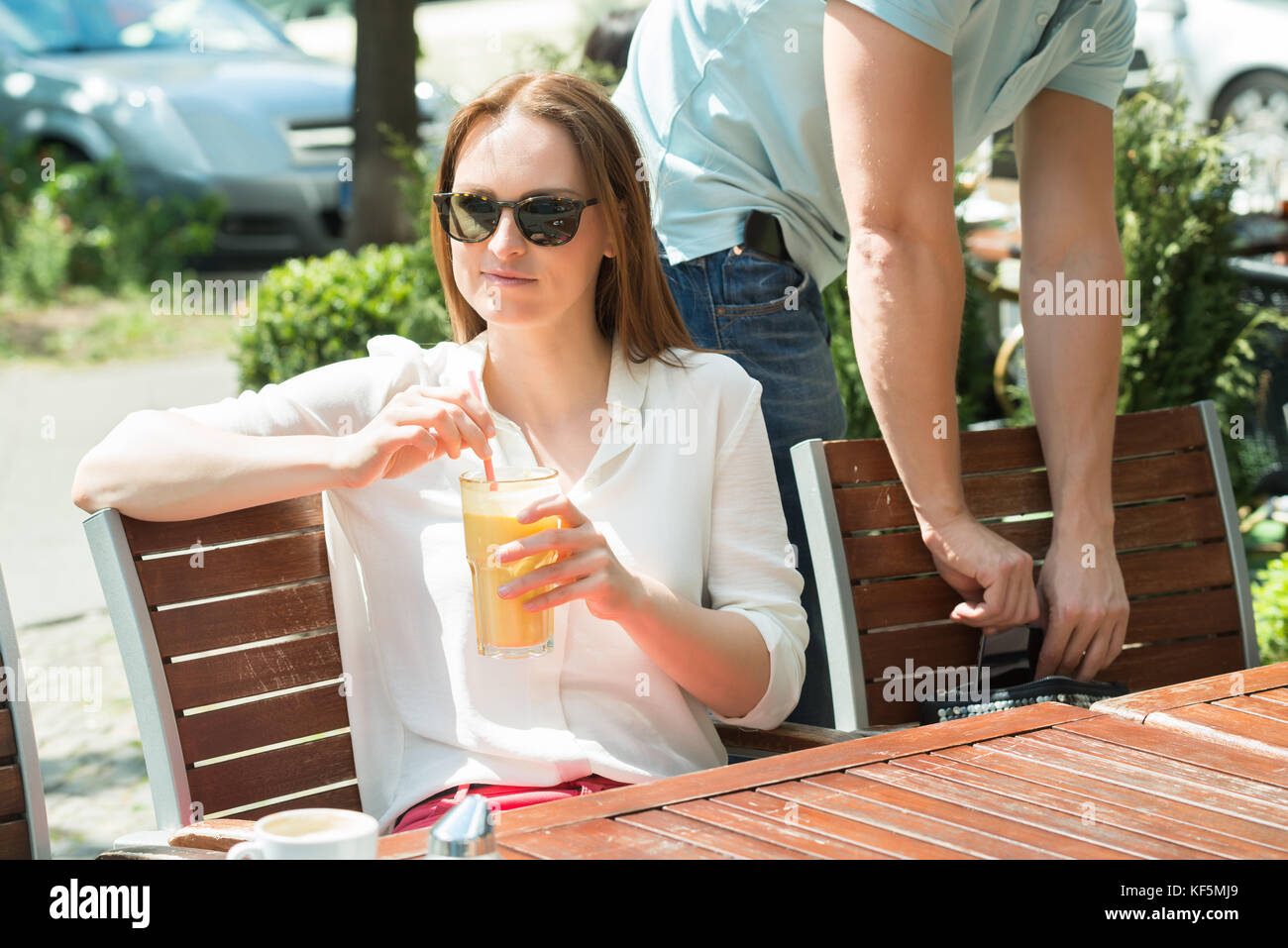 Vol voleur mâle téléphone mobile d'une jeune femme avec verre de jus Banque D'Images