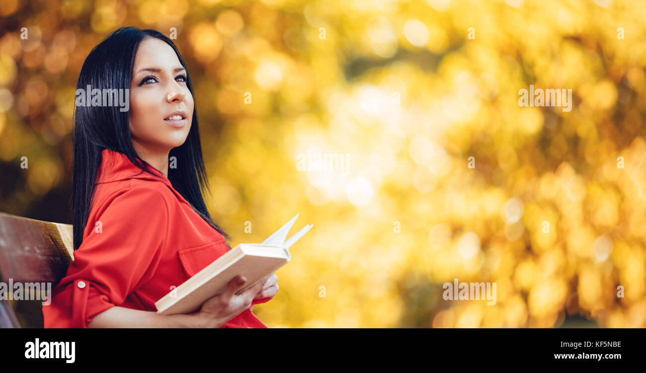 Belle jeune femme bénéficiant de couleurs d'automne forêt ensoleillée à la voiture et tenant un livre dans sa main. Banque D'Images