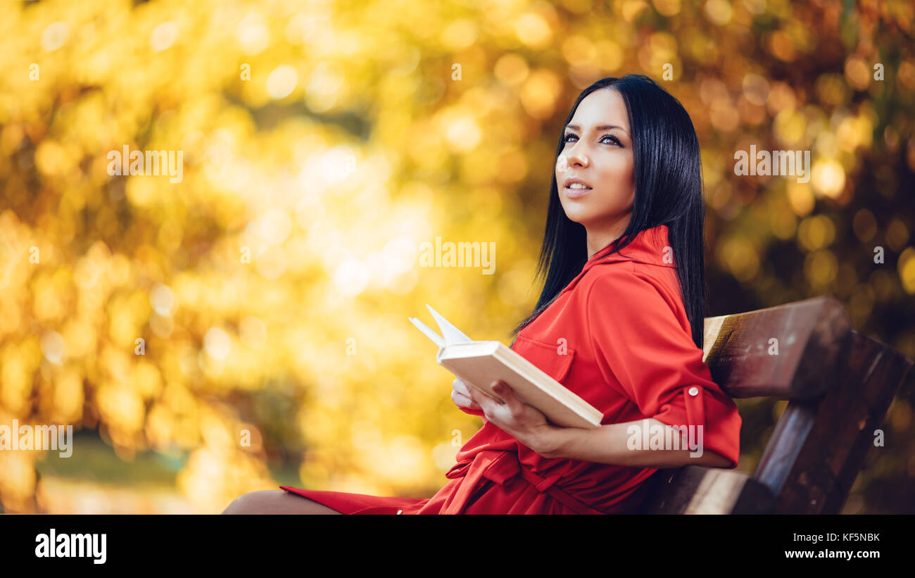 Belle jeune femme pensive bénéficiant dans couleurs d'automne forêt ensoleillée à la voiture et tenant un livre dans sa main. Banque D'Images