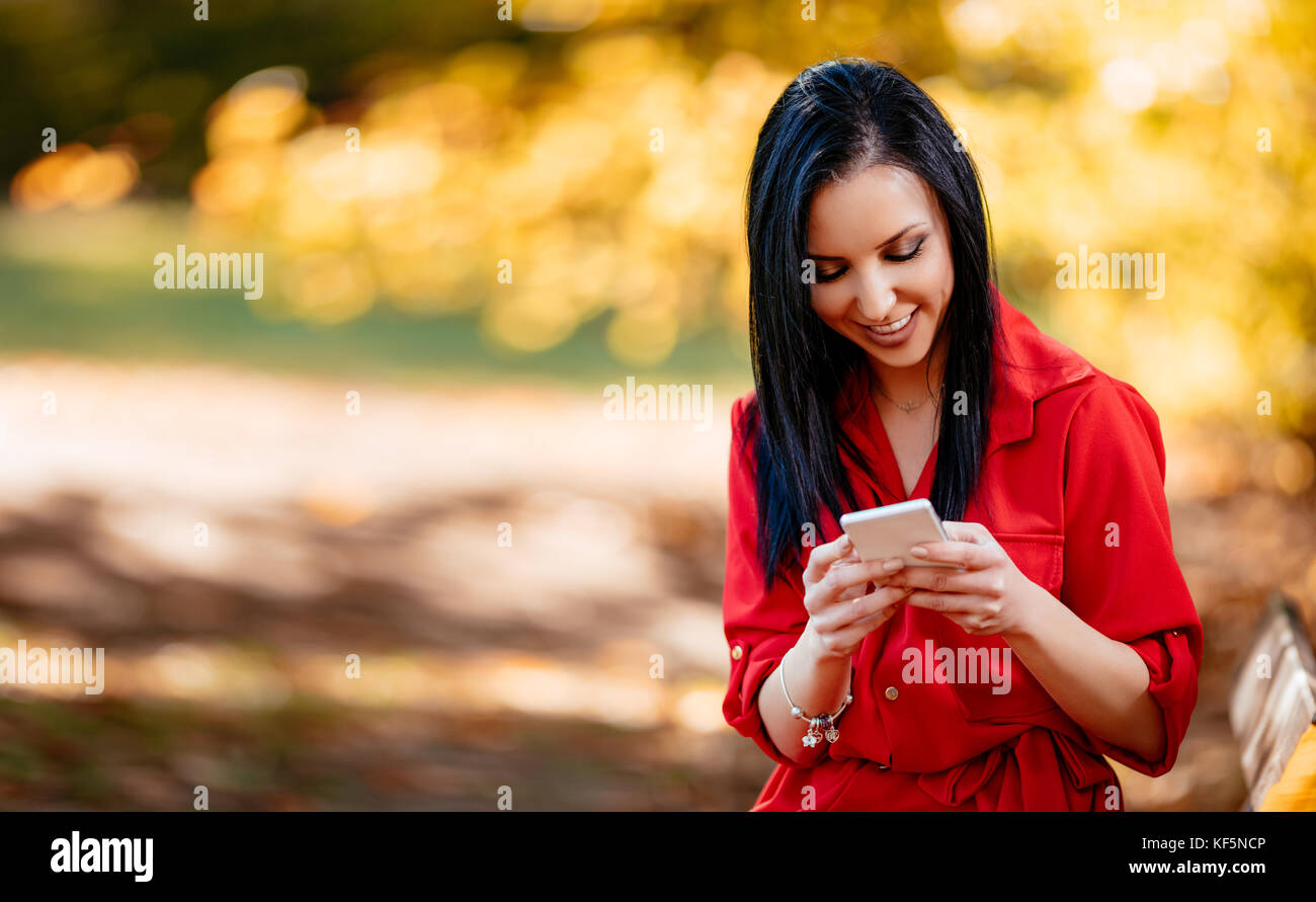 Happy young smiling woman reading message avec pleasant news sur smartphone à l'automne la nature. Banque D'Images