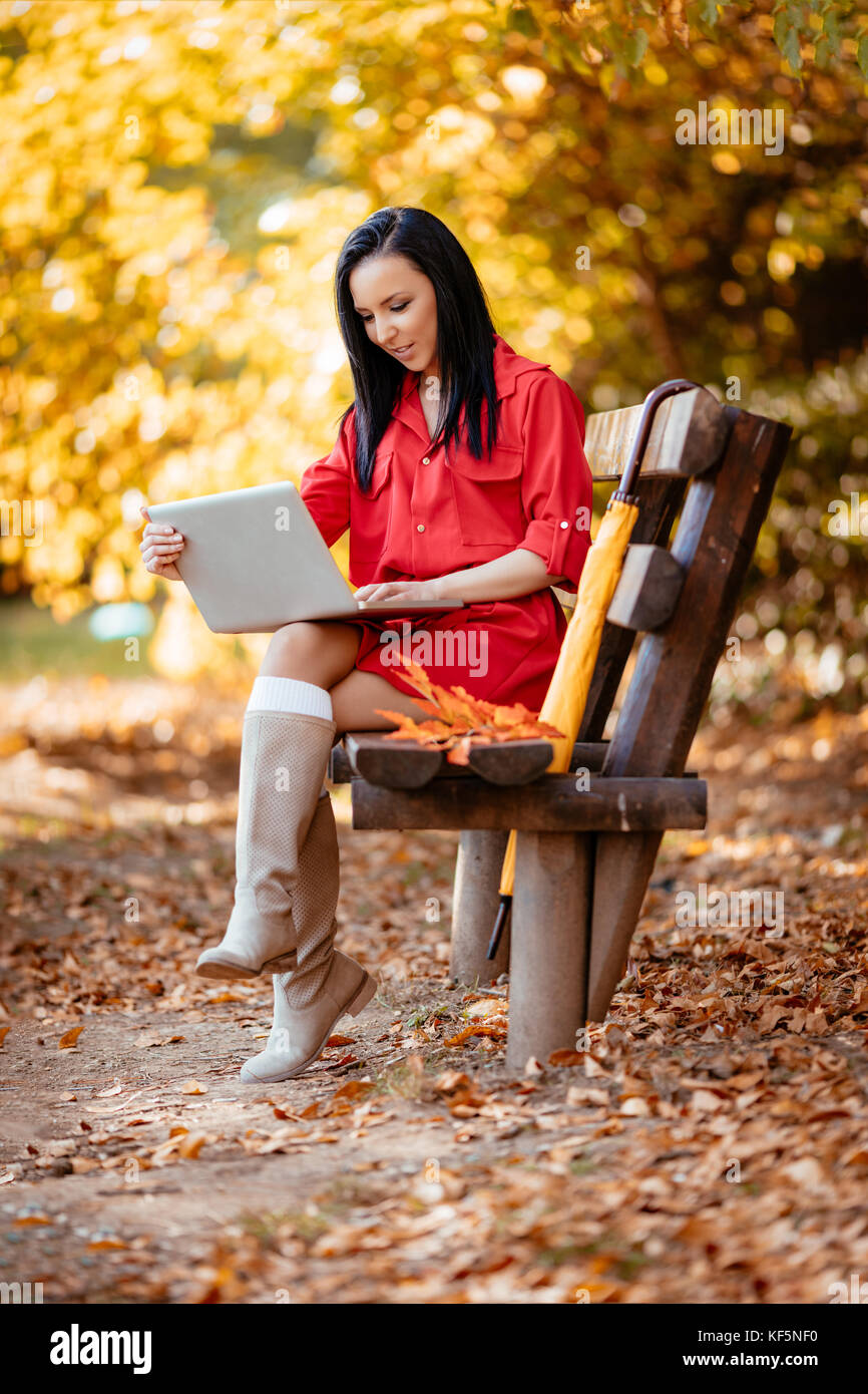 Jeune femme travaillant sur un ordinateur portable sur le banc du parc en automne. Banque D'Images