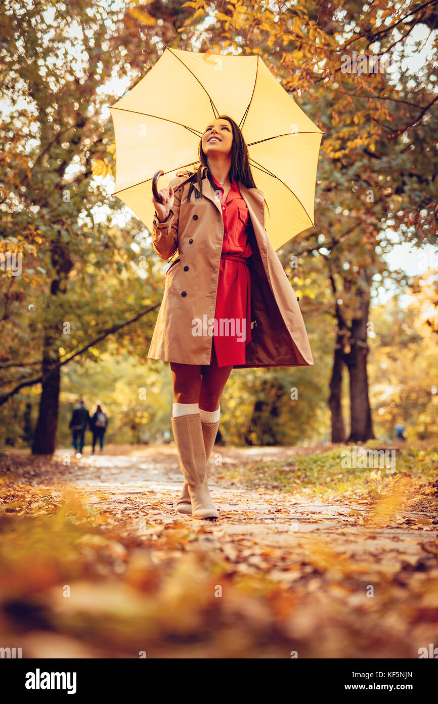 Heureux femme avec parapluie jaune en marche à beautifu parc ensoleillée d'automne. Banque D'Images