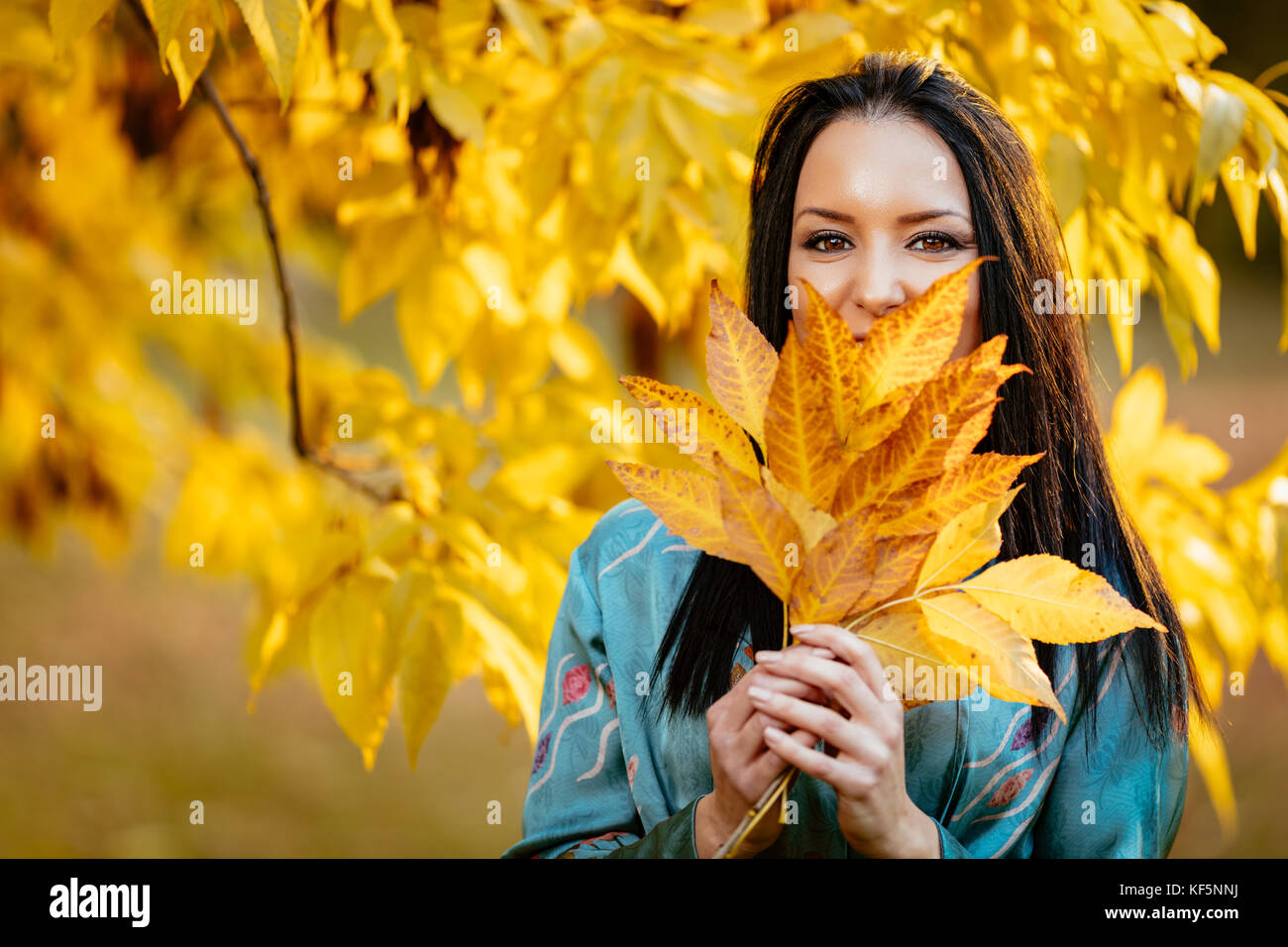 Beautiful happy woman holding les feuilles d'automne sur son visage dans le parc ensoleillé et souriant. looking at camera. Banque D'Images